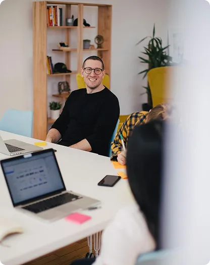 A mna sitting in an office whilst a meeting is going on. 